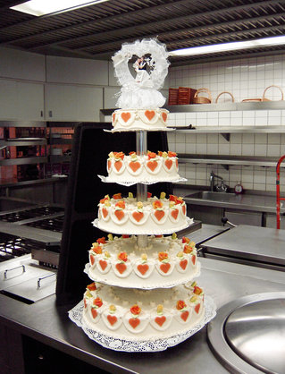 Eine mehrstöckige Hochzeitstorte aus Sahne, orangen Zuckerherzen, Blumen und einem Hochzeitspaar auf der Spitze