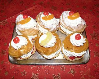 Sechs Windbeutel mit einem Topping aus Sahne und Früchten sind auf einem silbernen Tablett platziert